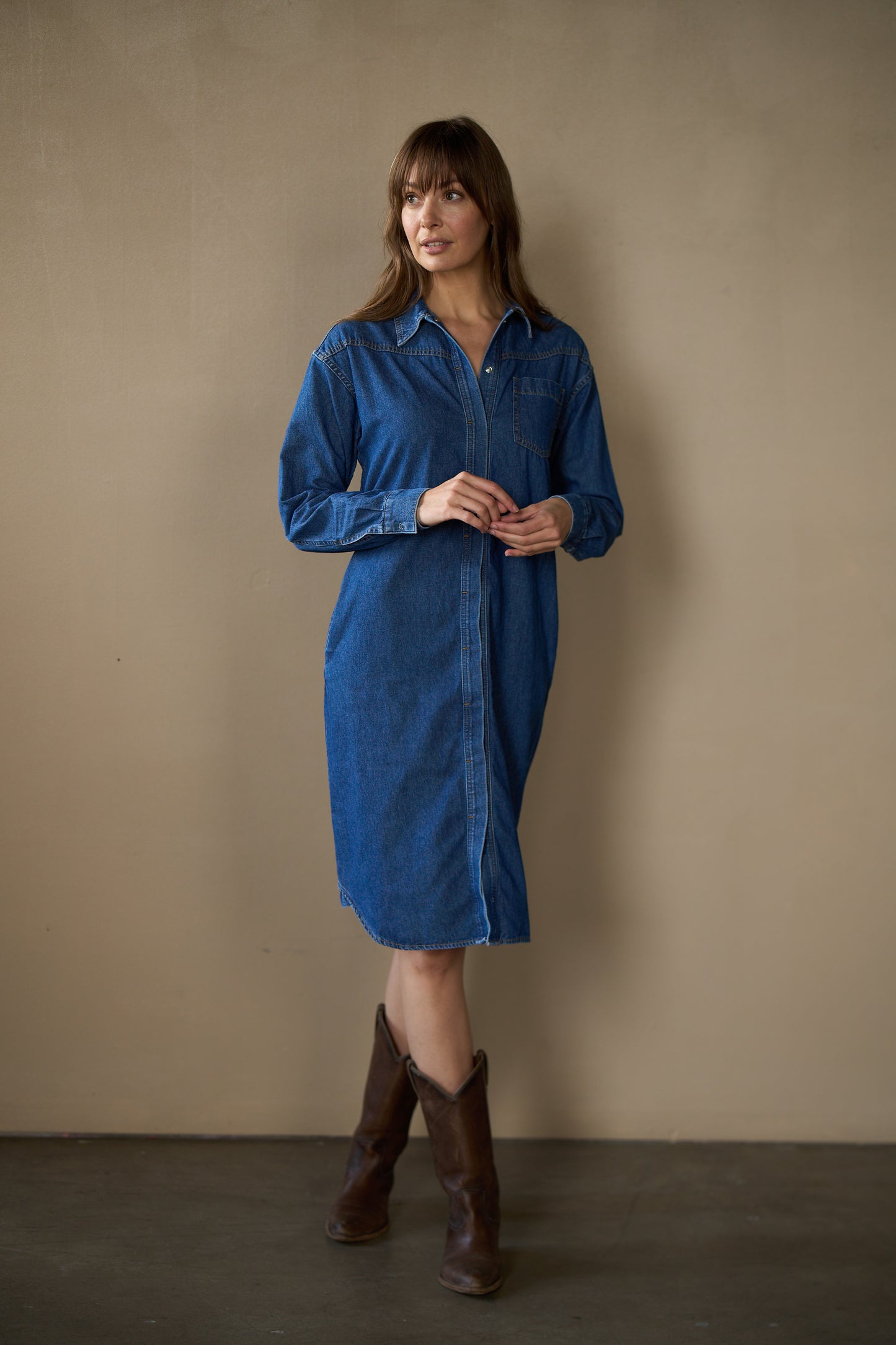 Woman wearing a blue dress standing against a beige wall.