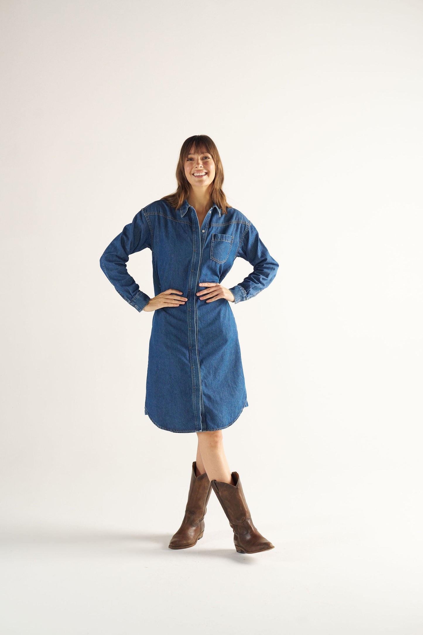 Woman wearing a blue denim dress and brown boots on a white background