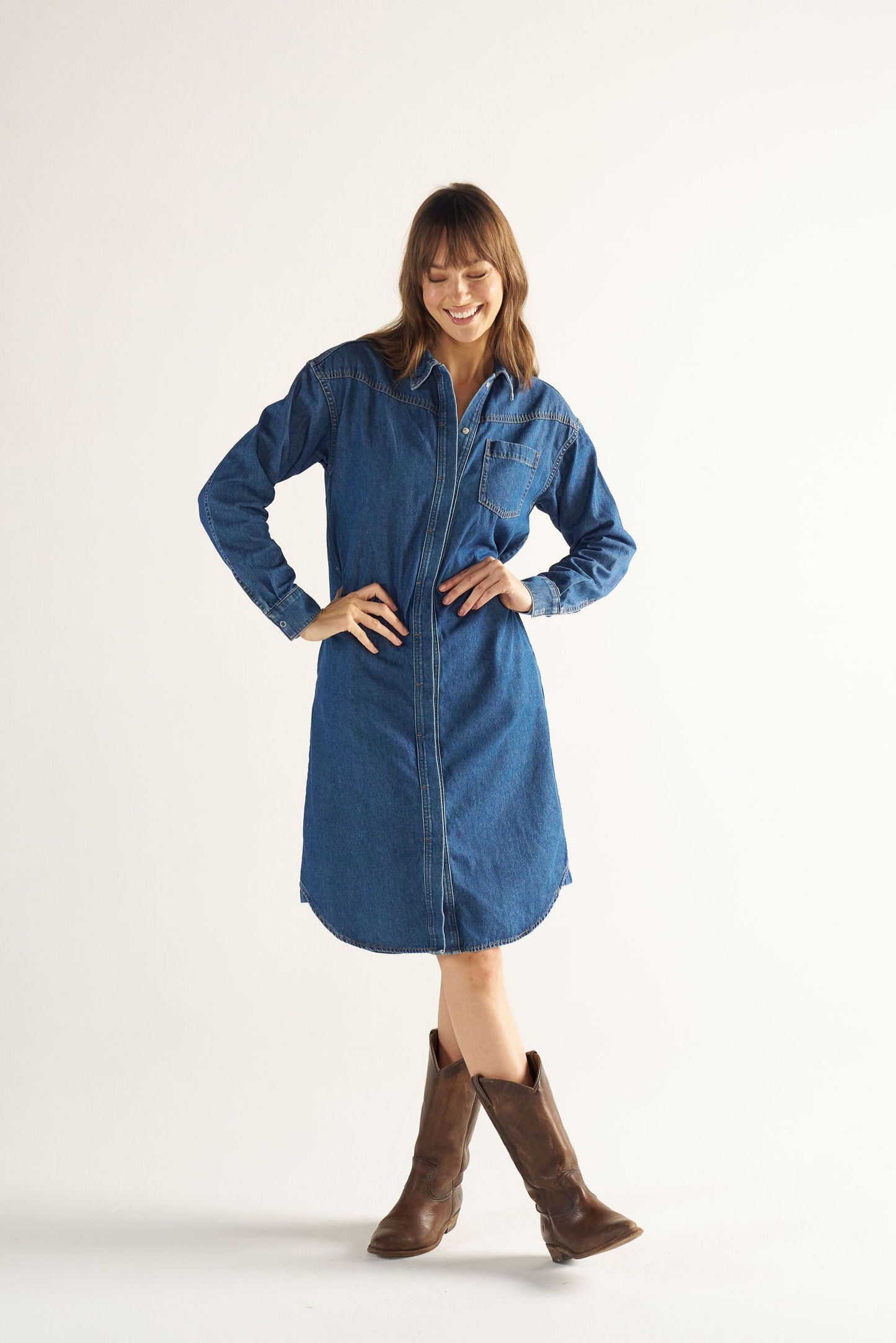 Woman wearing a blue denim dress with brown boots on a white background