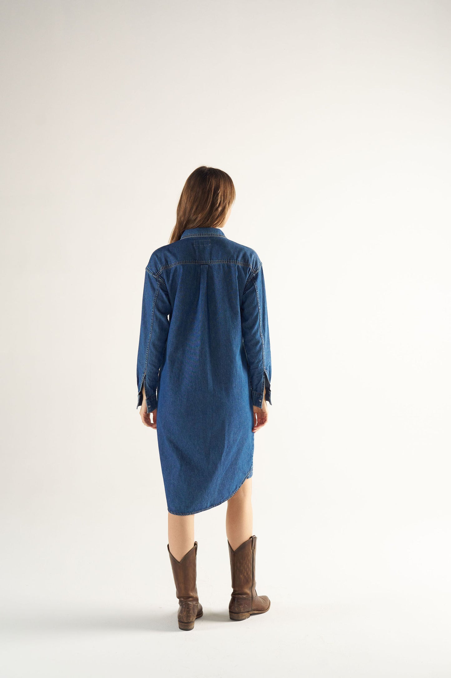 Woman wearing a blue denim dress and brown boots on a white background