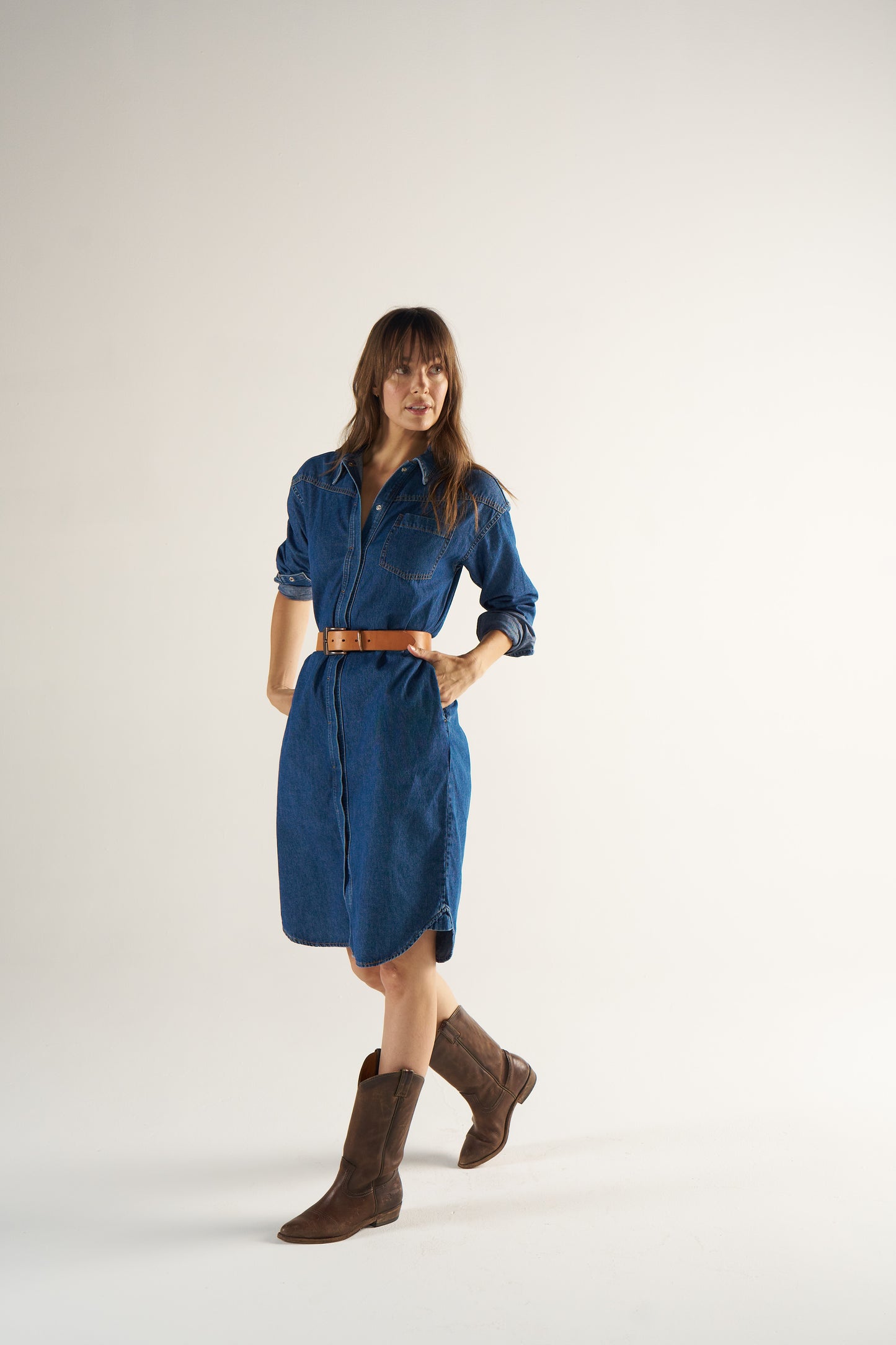 Woman wearing a blue dress with a brown belt and brown boots on a white background