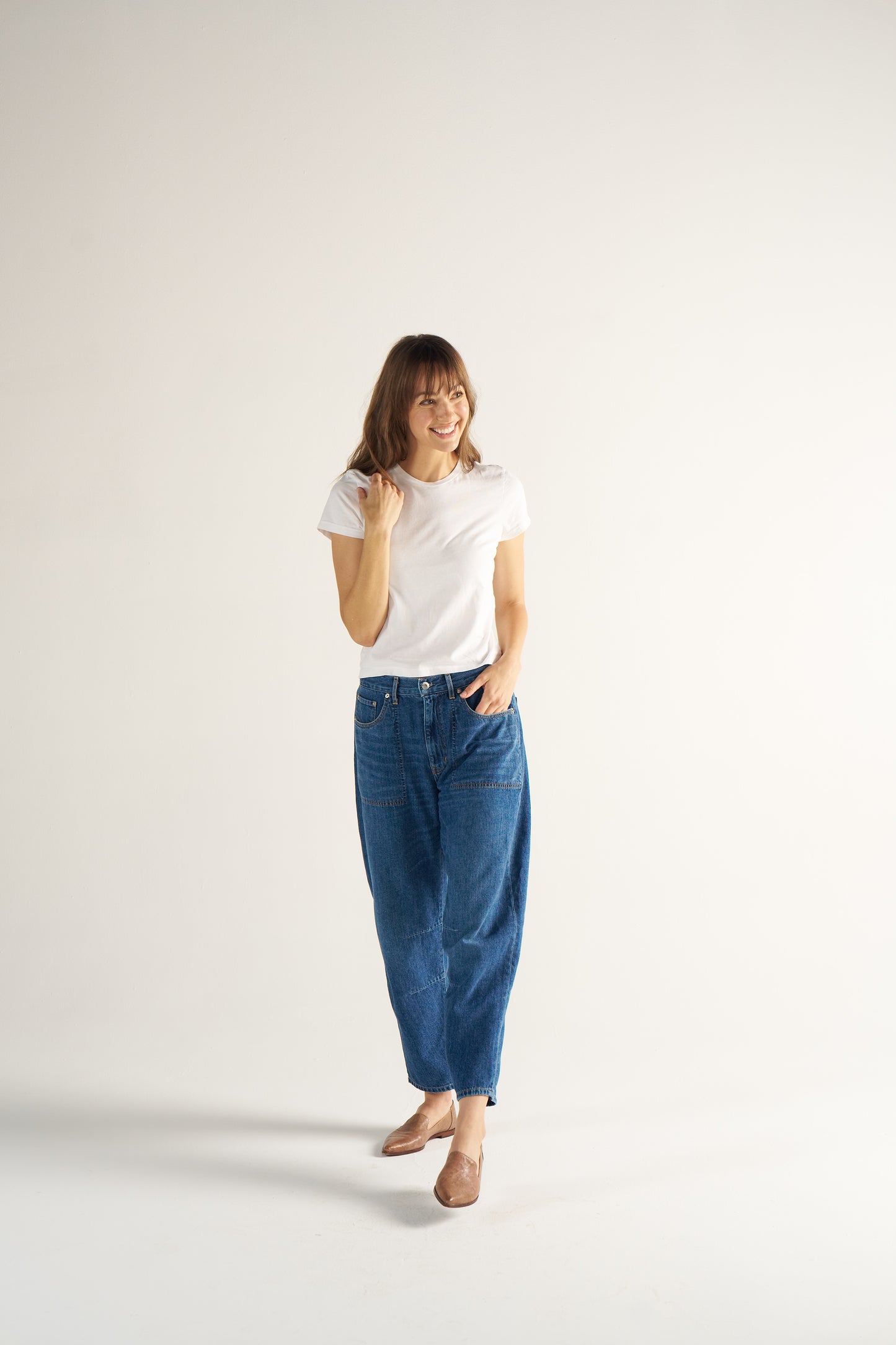 Woman wearing a white t-shirt and blue jeans on a plain background