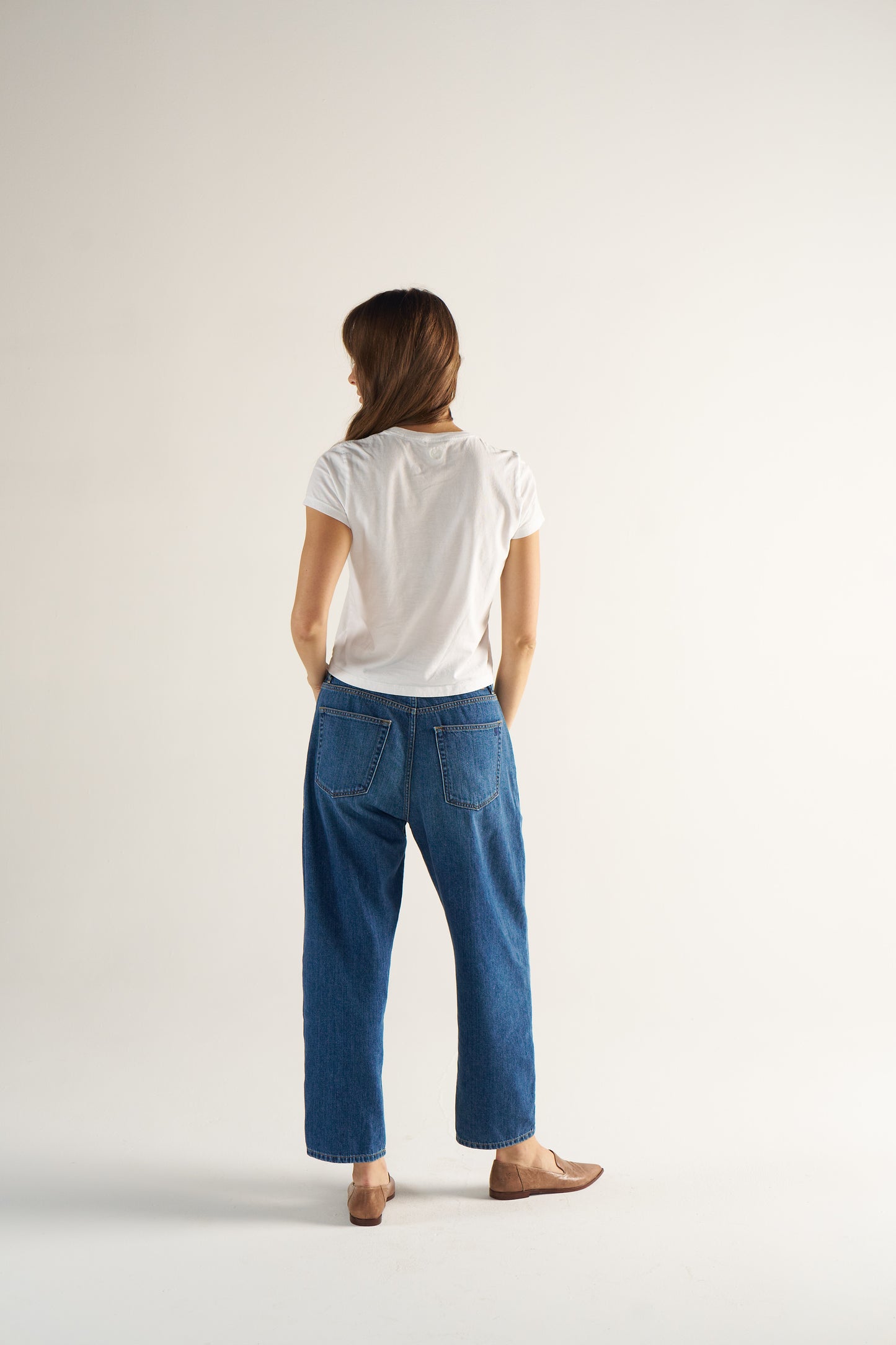 Woman wearing a white t-shirt and blue jeans standing against a plain background
