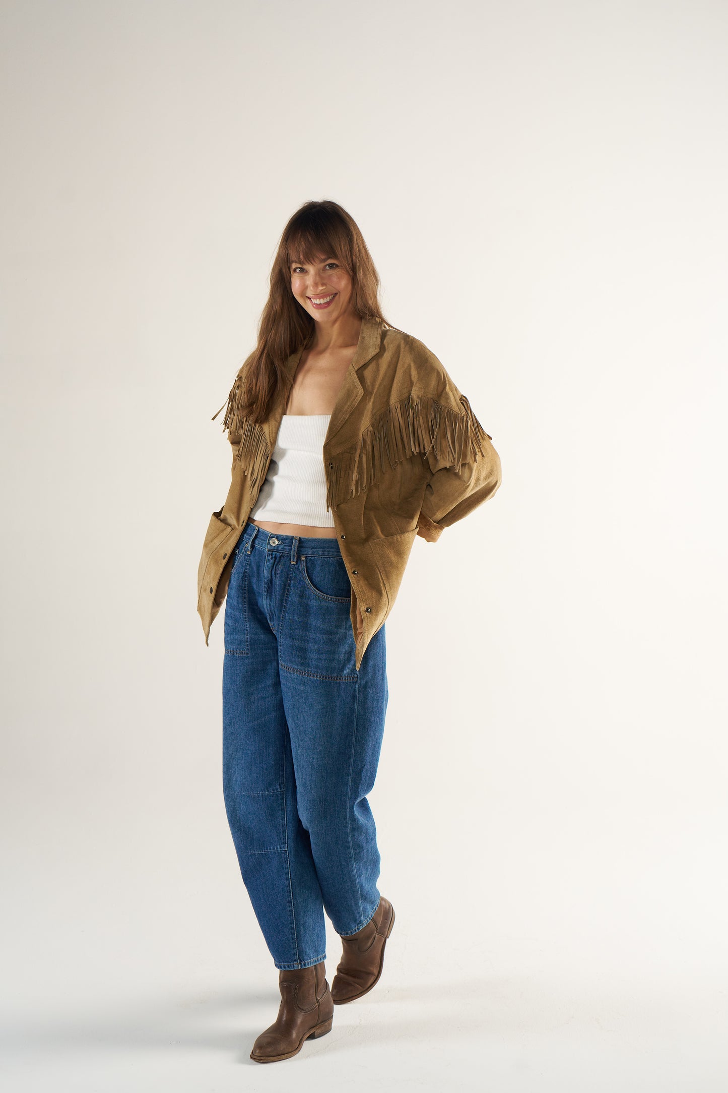 Woman wearing a brown jacket, white top, blue jeans, and brown boots on a white background