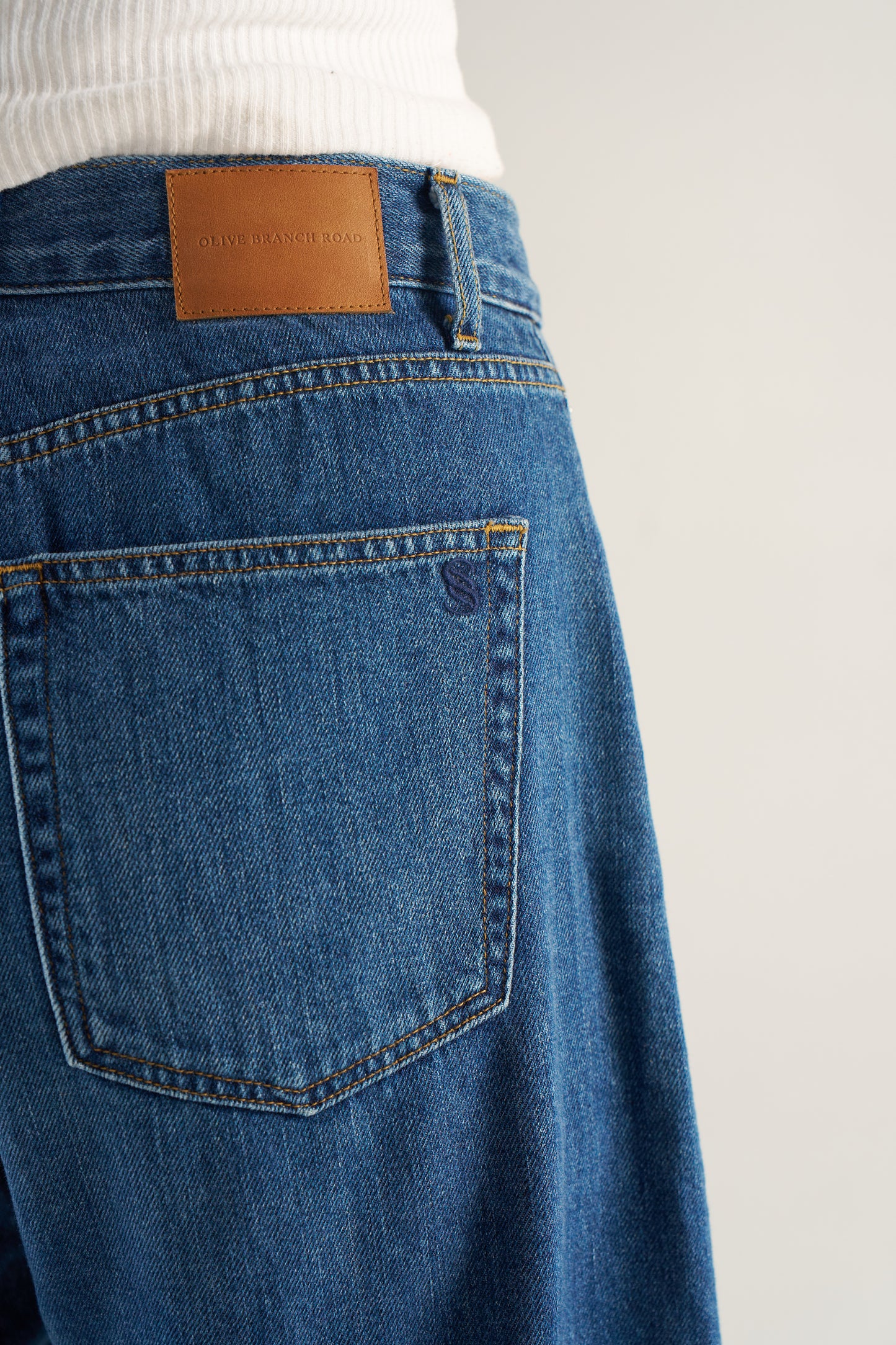 Close-up of blue jeans with a leather patch brand label on a white background