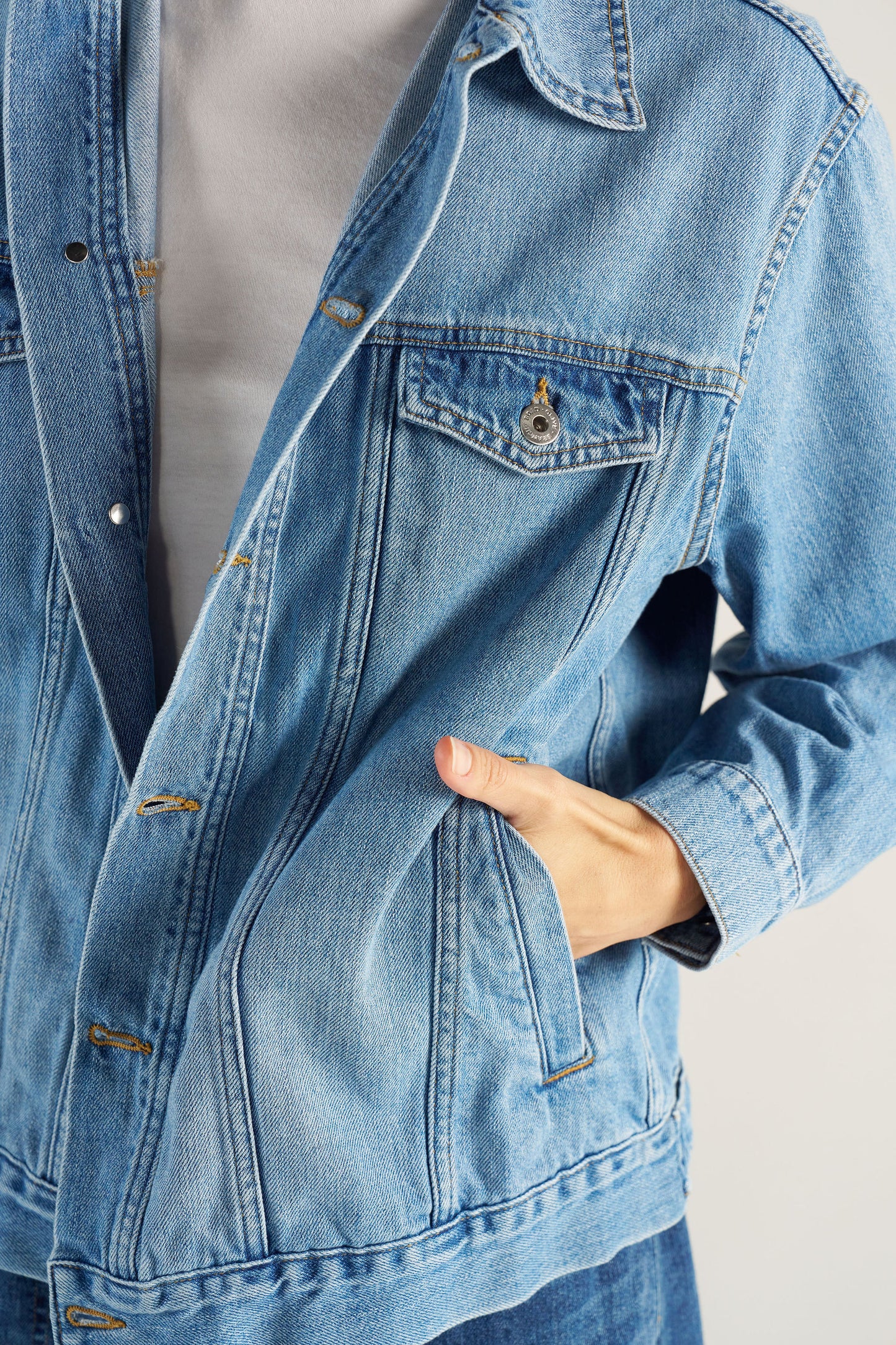Close-up of a blue denim jacket with a hand touching the fabric with hand in pocket.