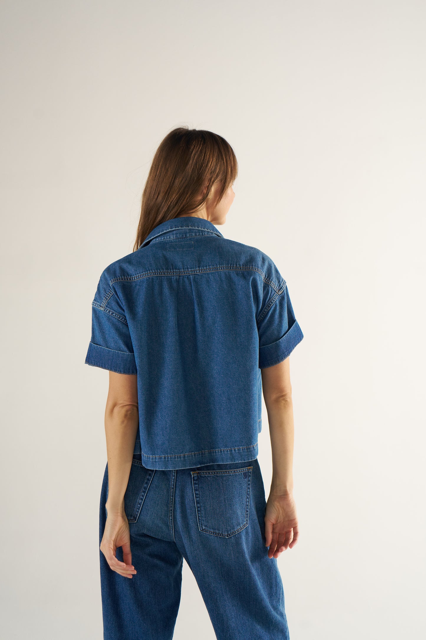 Person wearing a blue denim jacket and pants on a plain background