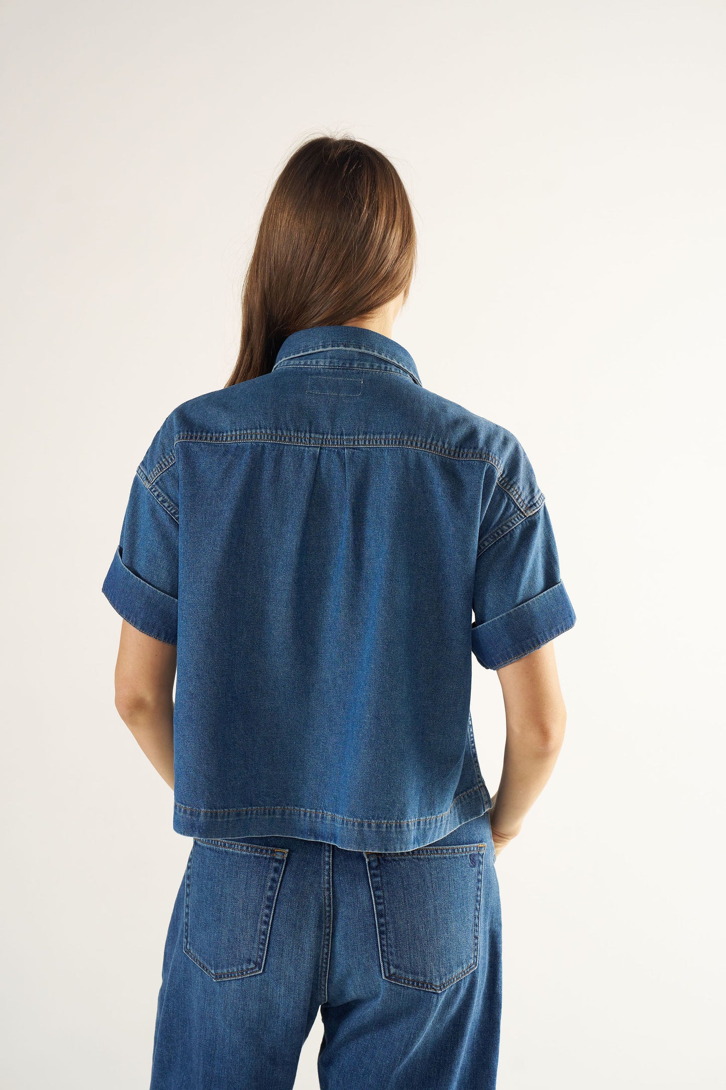 Woman wearing a blue denim jacket and pants on a white background