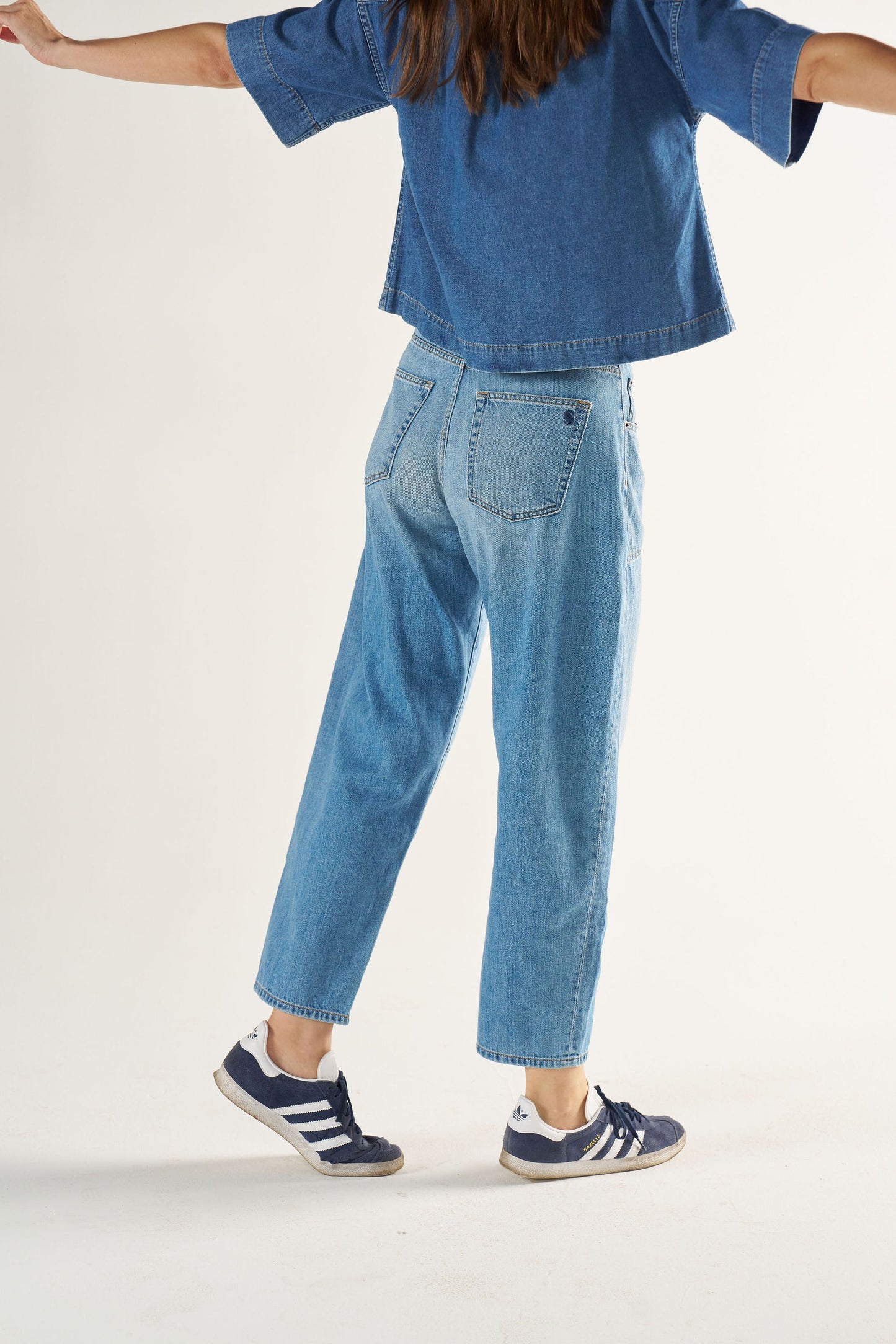 Woman wearing a blue denim outfit with Adidas shoes on a white background
