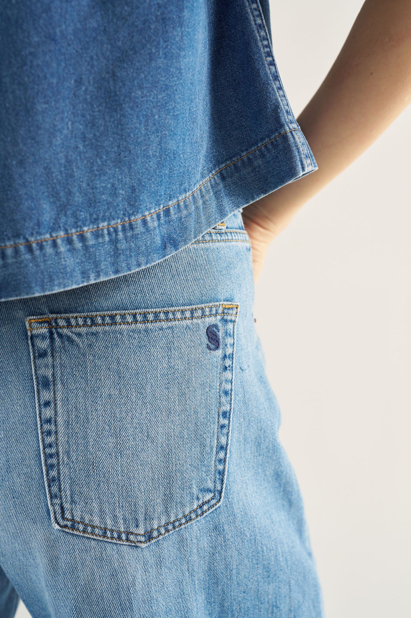 Close-up of a person wearing blue jeans with a visible brand logo on a light background