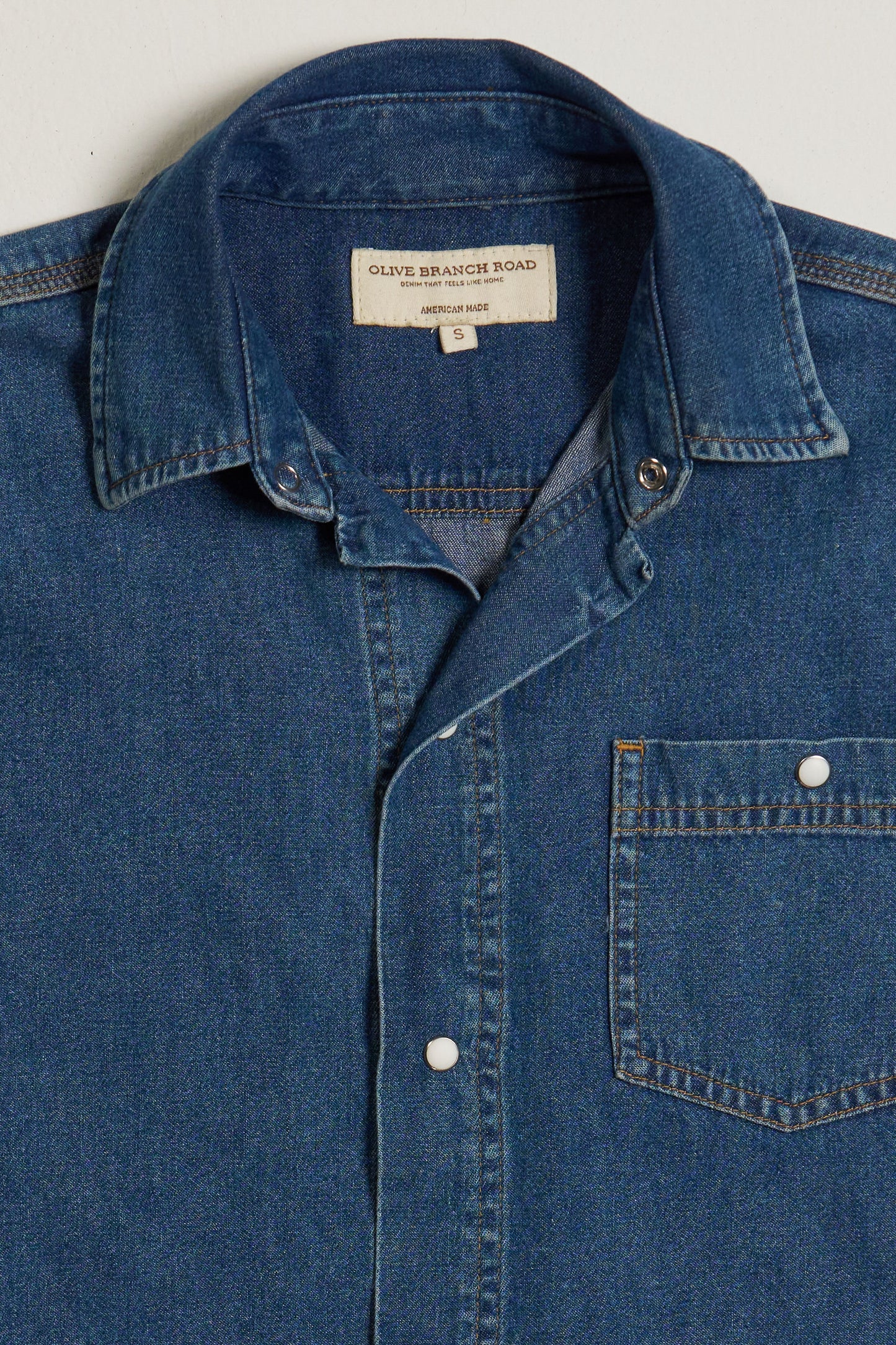 Blue denim shirt with a collar, pearl snaps and a pocket on a light gray background