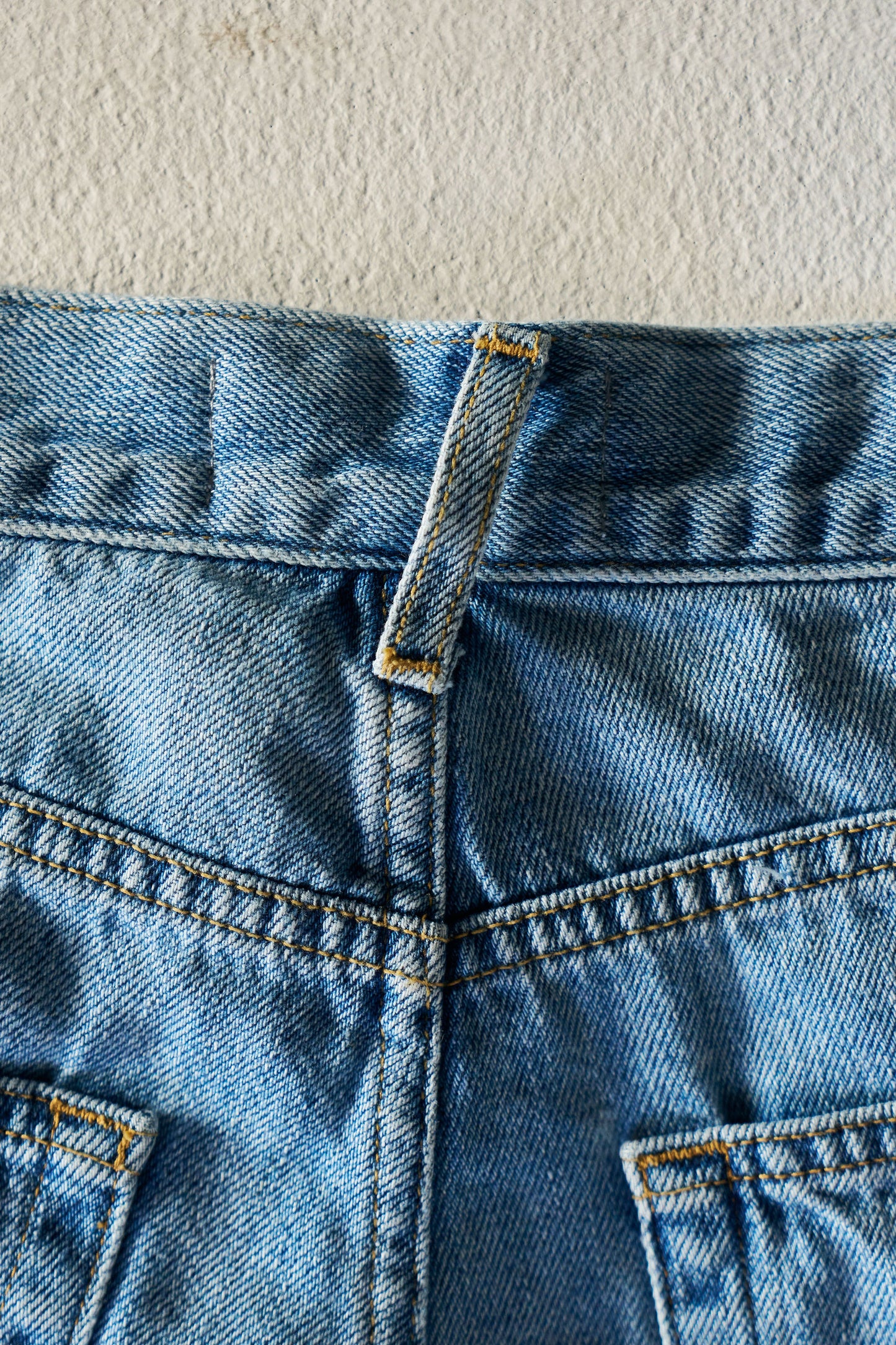 Close-up of blue denim jeans with stitching details on a textured beige background