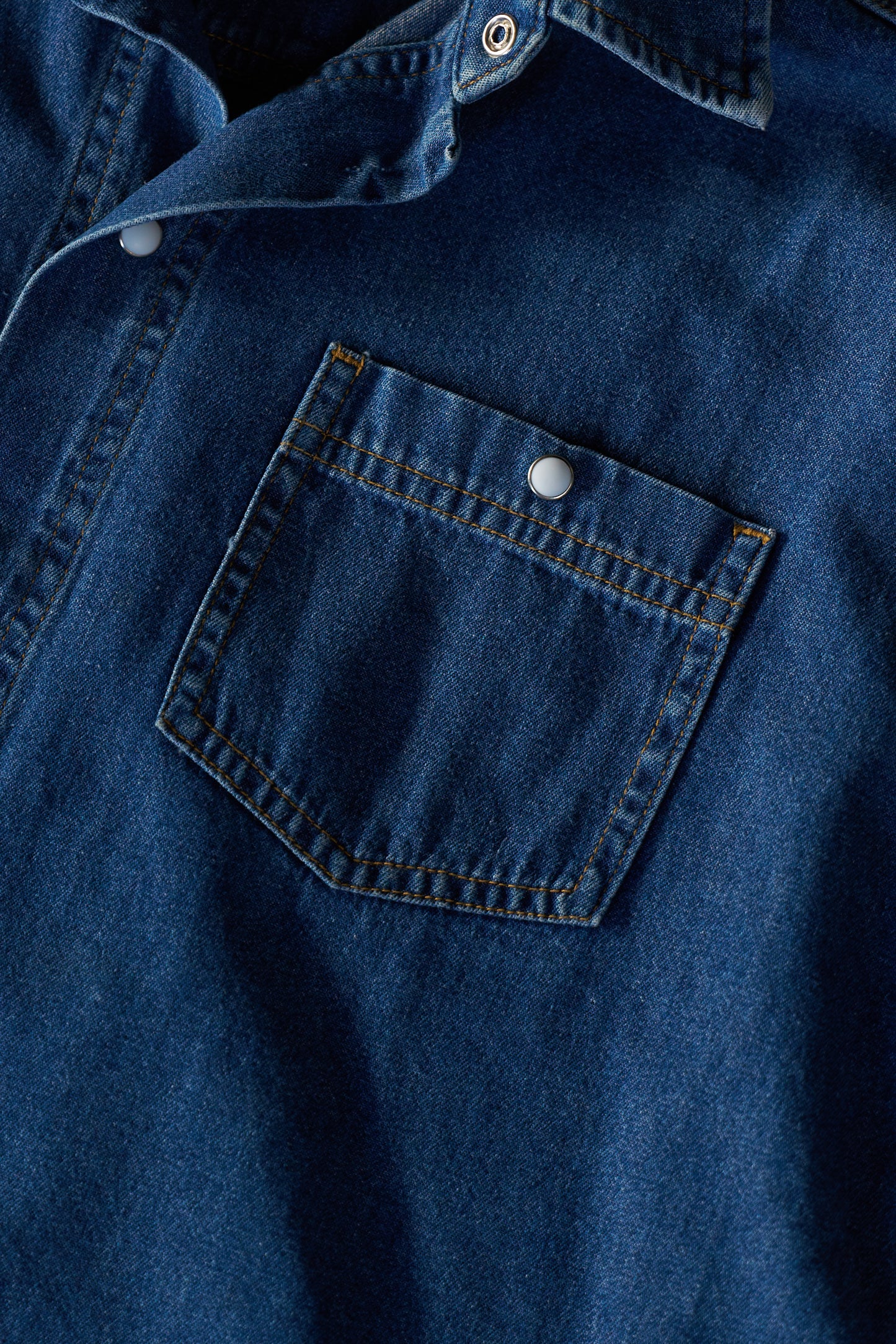 Close-up of a blue denim shirt with a pocket and pearl snap button details.