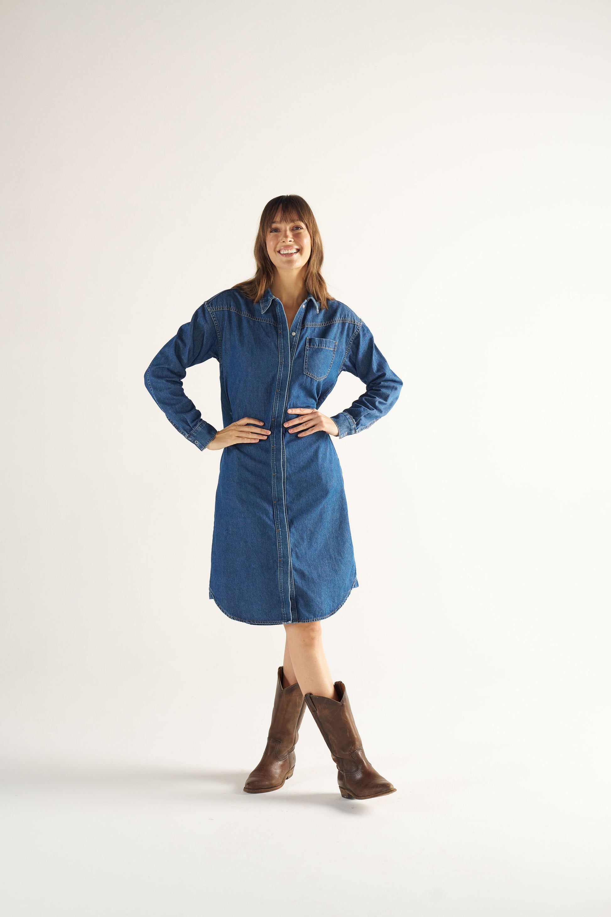 Woman wearing a blue denim dress and brown boots on a white background