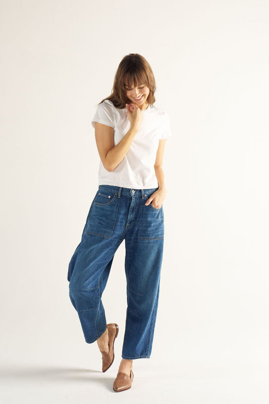 Woman wearing a white t-shirt and blue jeans on a plain background